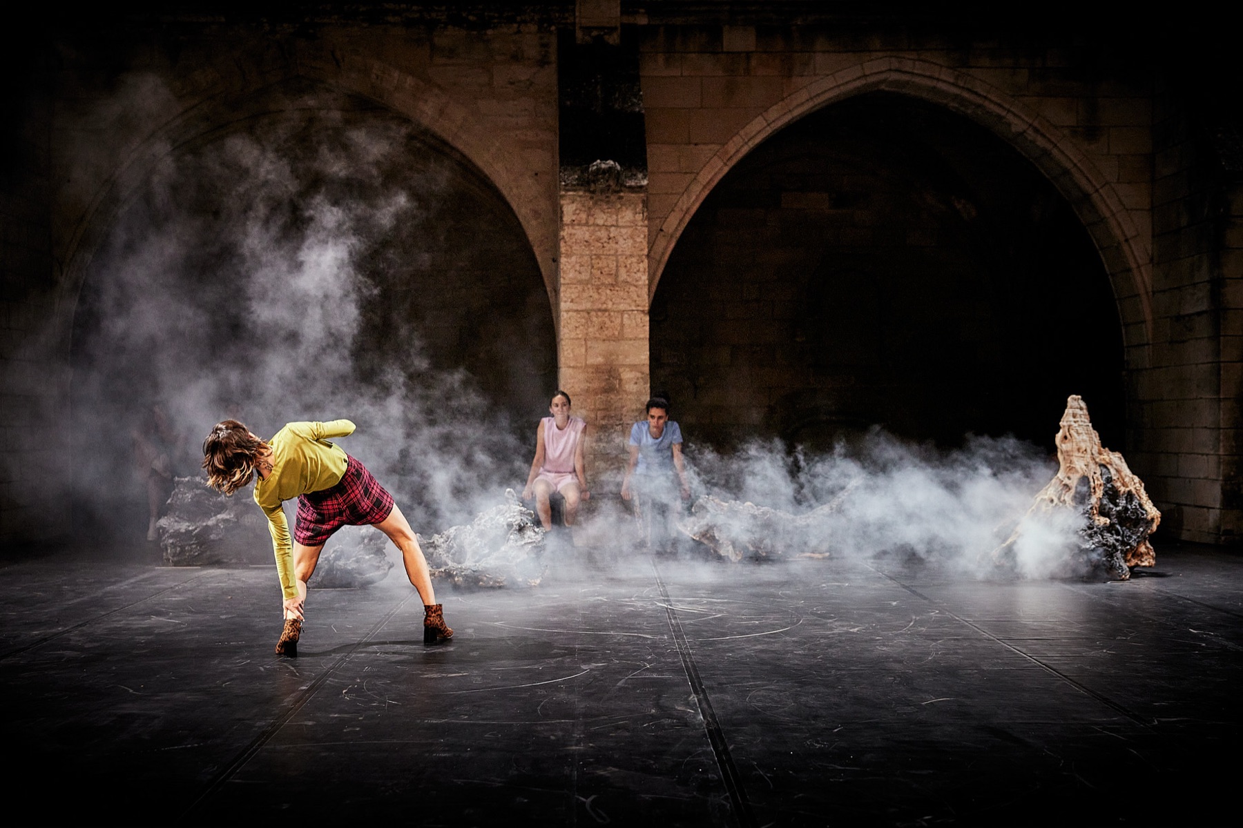 Bailarinas en un escenario con humo bajo arcos de piedra