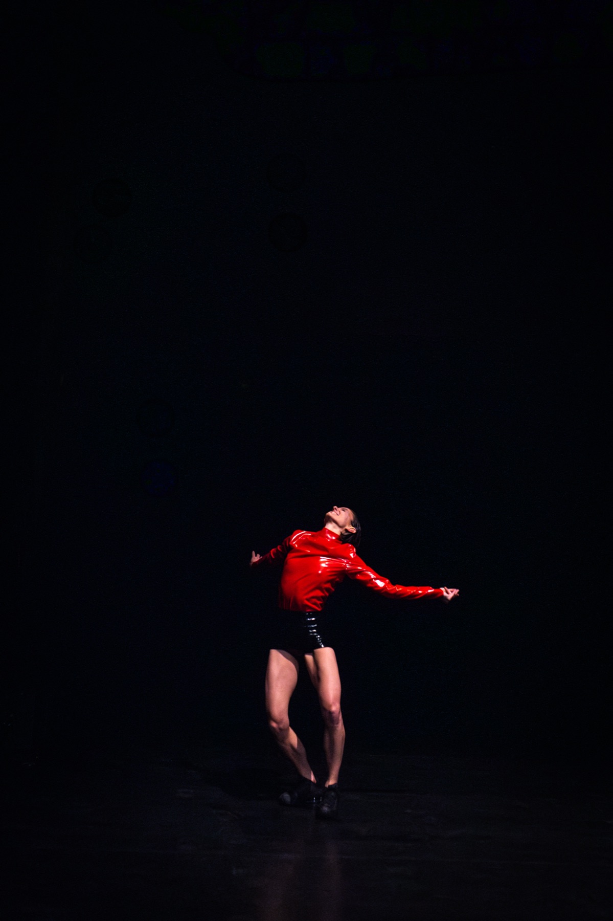 Lucía con chaqueta roja de látex, sola en un escenario oscuro